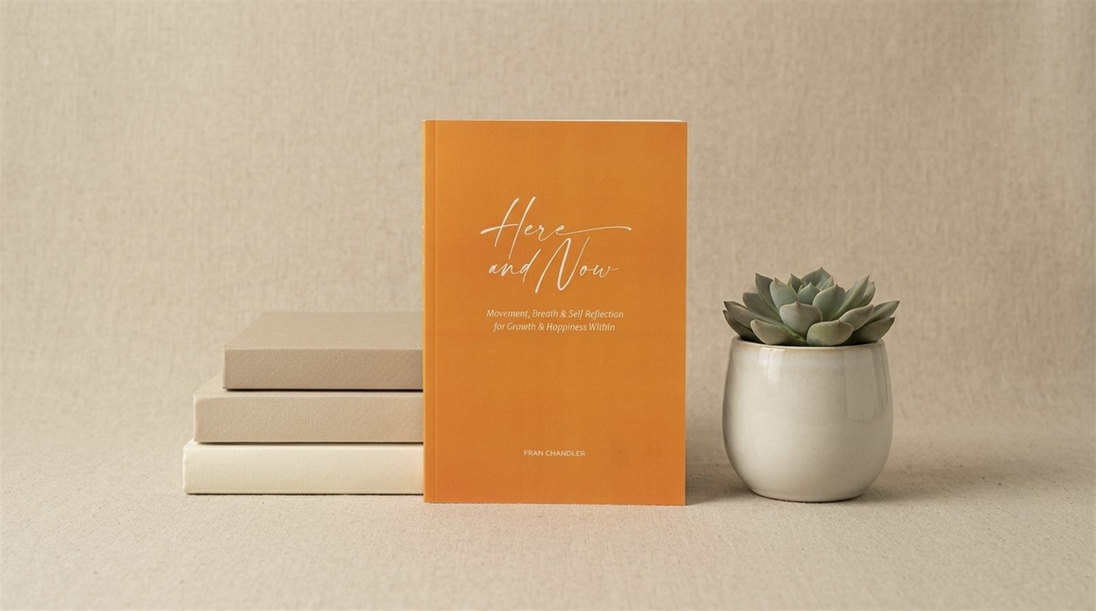 Here and Now styled on a shelf beside a small succulent and stacked notebooks