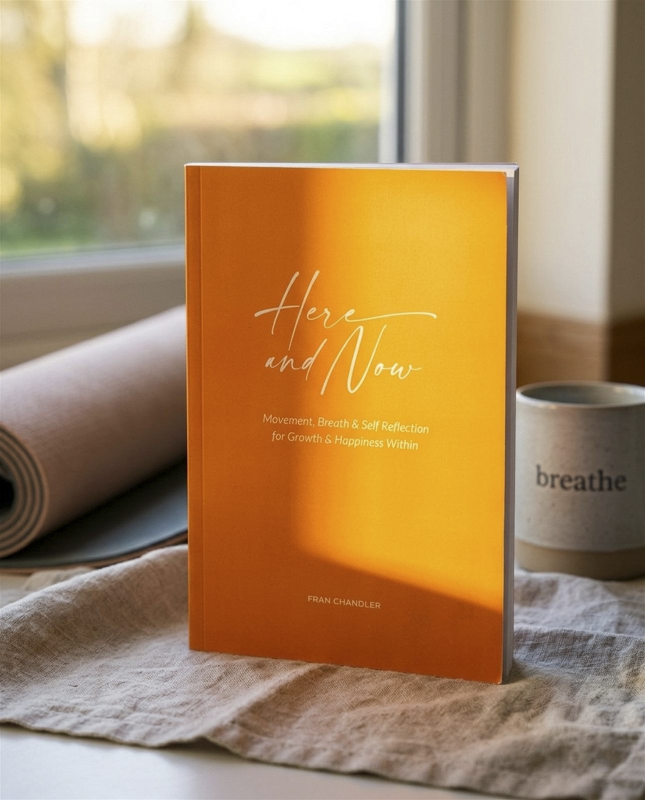 Here and Now standing on a table beside a rolled yoga mat and a mug that reads breathe
